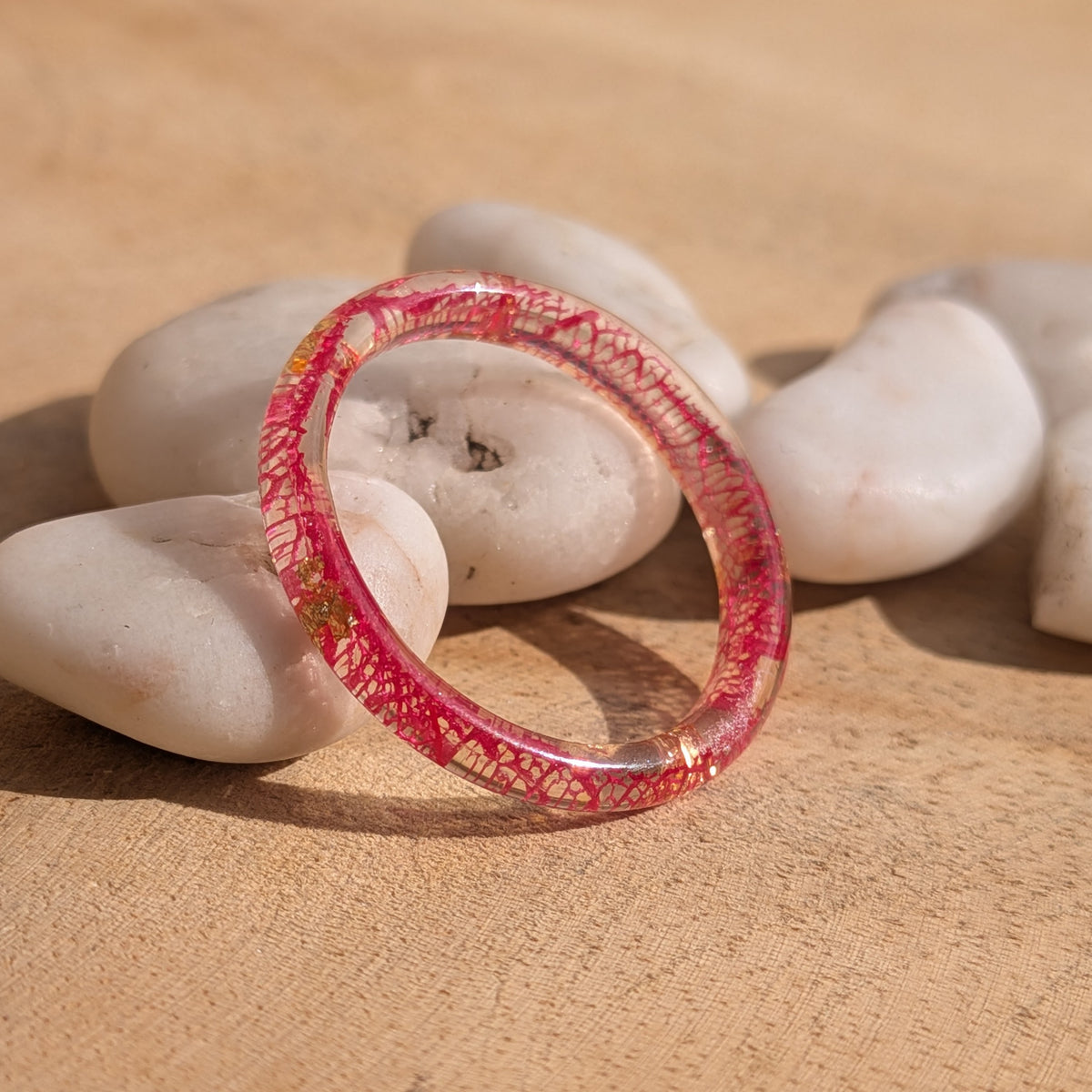 Thin red skeleton leaf resin ring with copper flakes standing upright against white pebbles on wood, EL-Creations