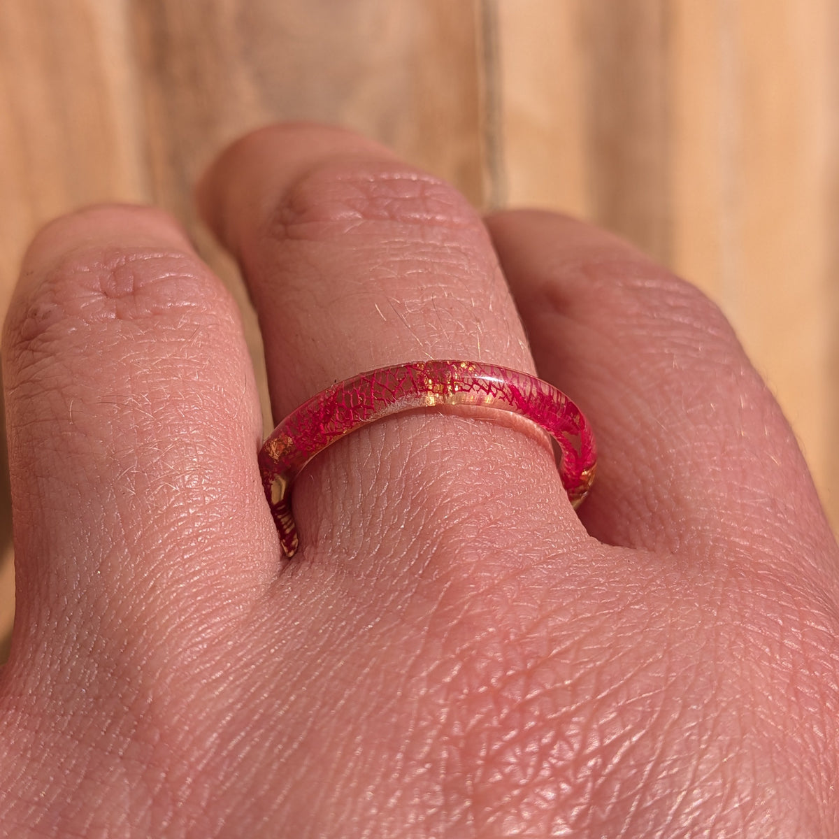 Front macro view of a red skeleton leaf resin ring worn on a finger, showing copper flakes beneath its glossy surface, EL-Creations