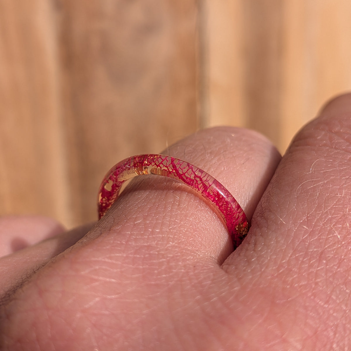 Side macro close-up of red skeleton leaf veins and copper flakes inside a delicate resin ring worn on a finger, EL-Creations