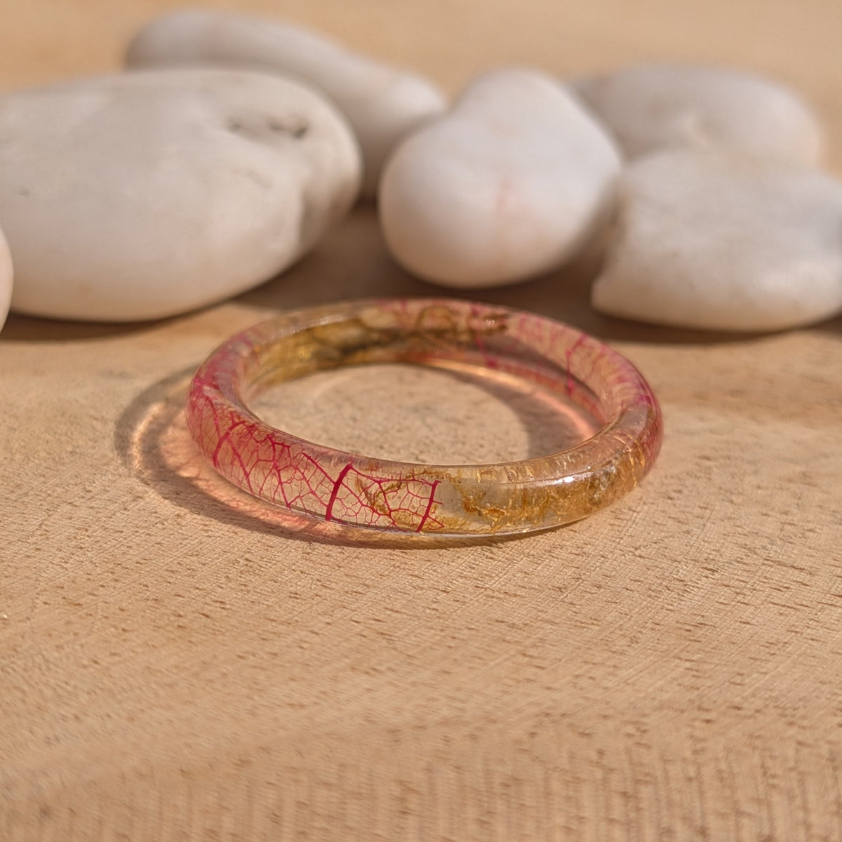 Pink skeleton leaf and moss resin ring lying flat on wood with white stones in the background, EL-Creations