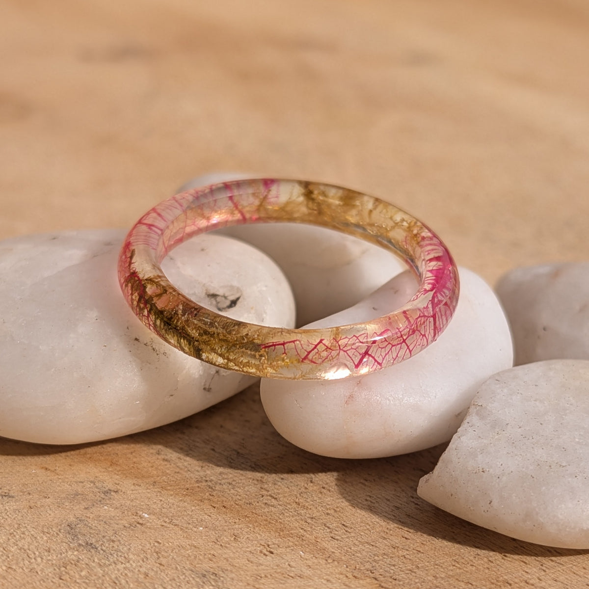 Botanical resin ring with pink skeleton leaf and moss balanced on white stones, showing its rounded band, EL-Creations