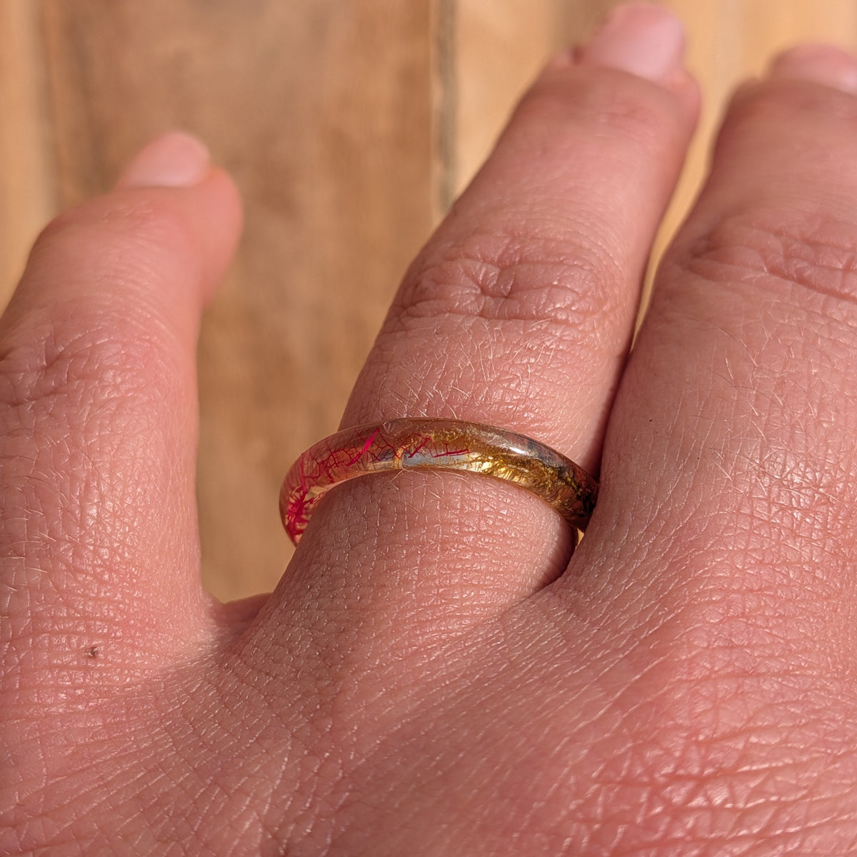 Delicate pink skeleton leaf and moss resin ring worn on a finger, viewed from above in sunlight, EL-Creations
