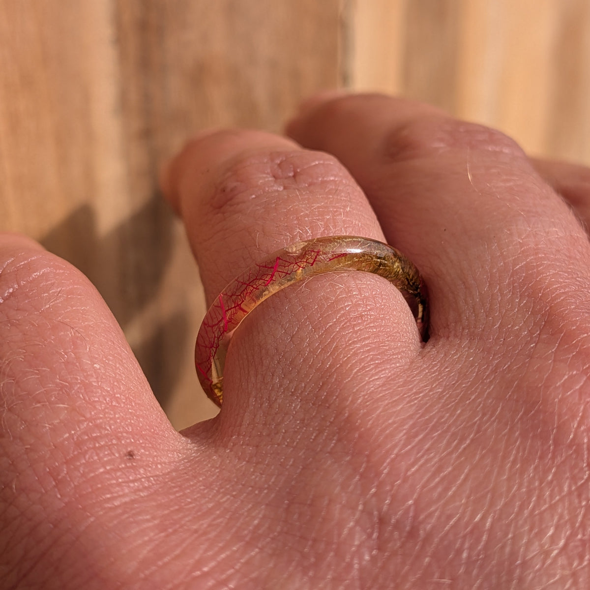 Angled close-up of pink skeleton leaf veins inside a thin resin ring worn on a finger, EL-Creations