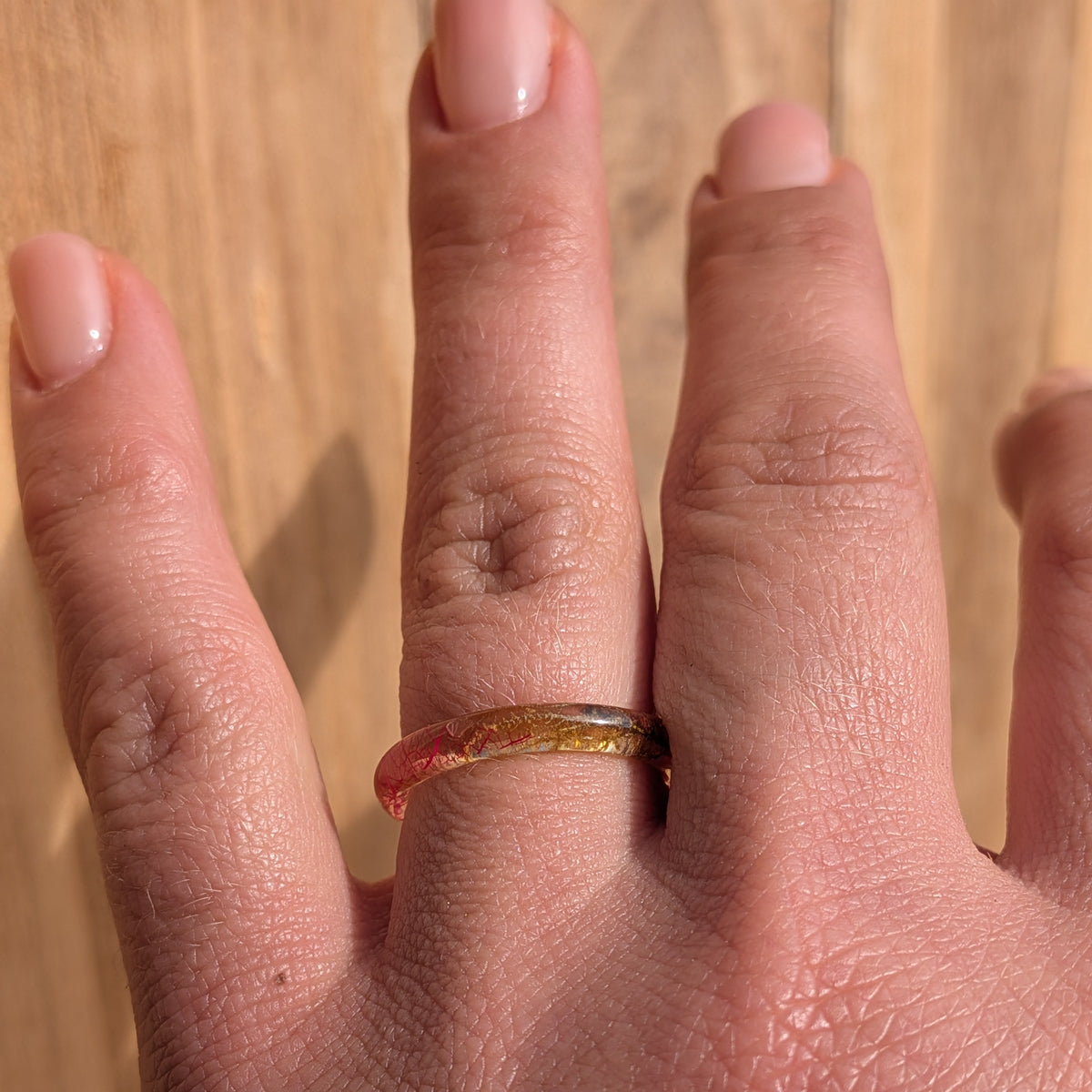 Thin botanical resin ring with pink skeleton leaf and moss worn on an outstretched hand against a wooden background, EL-Creations