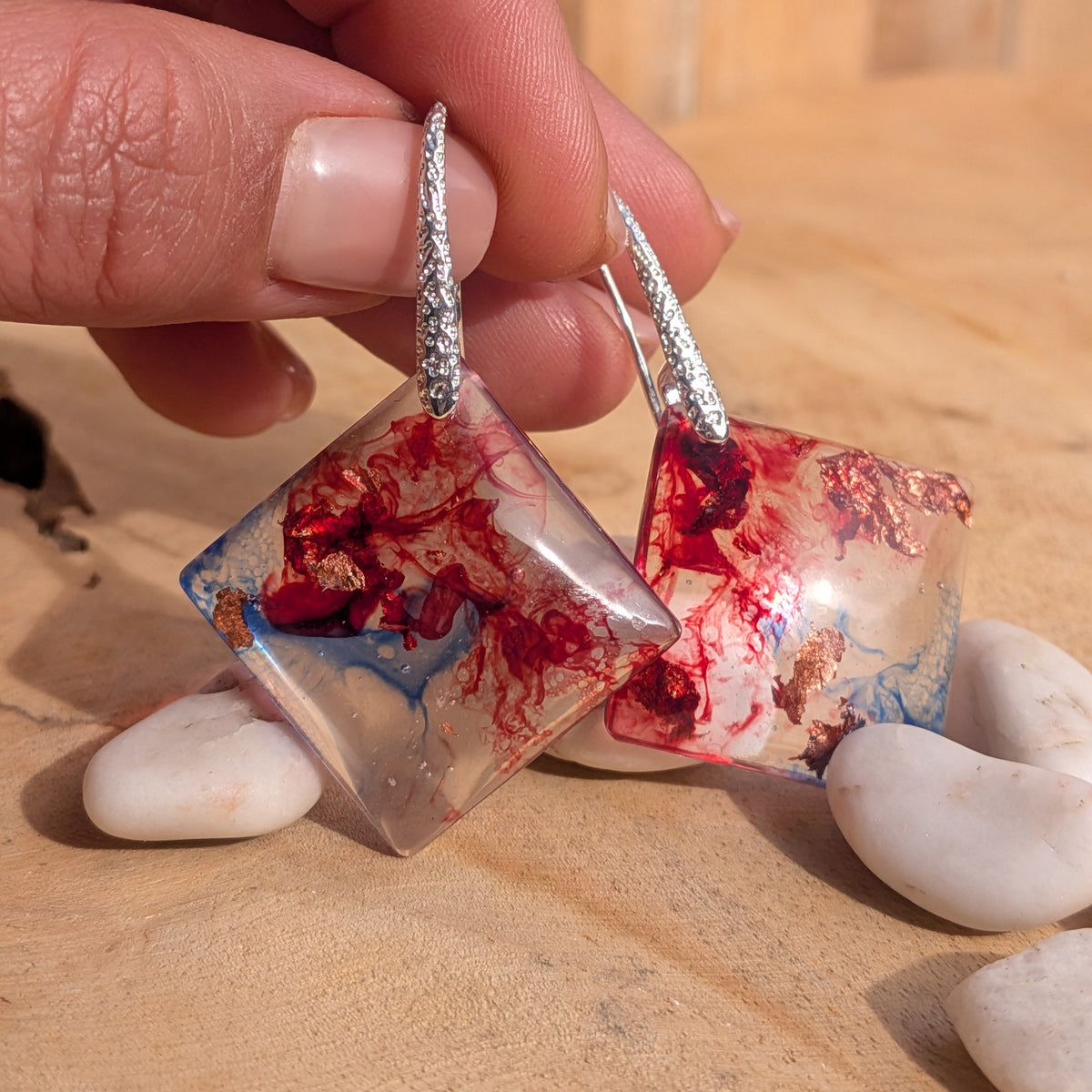 Red and blue geometric resin earrings held above white stones, EL-Creations

