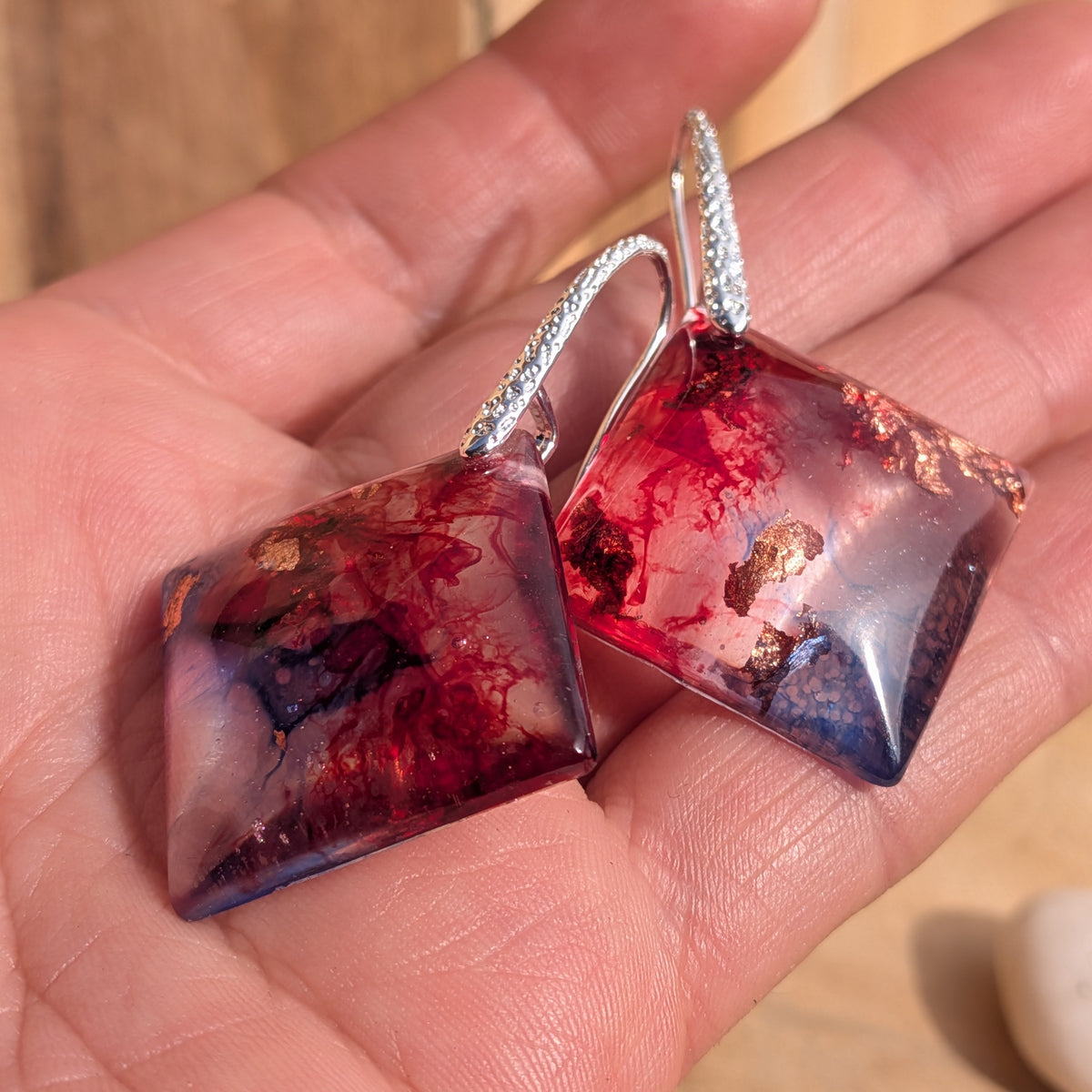 Pair of crimson blue square resin earrings displayed on an open palm, EL-Creations