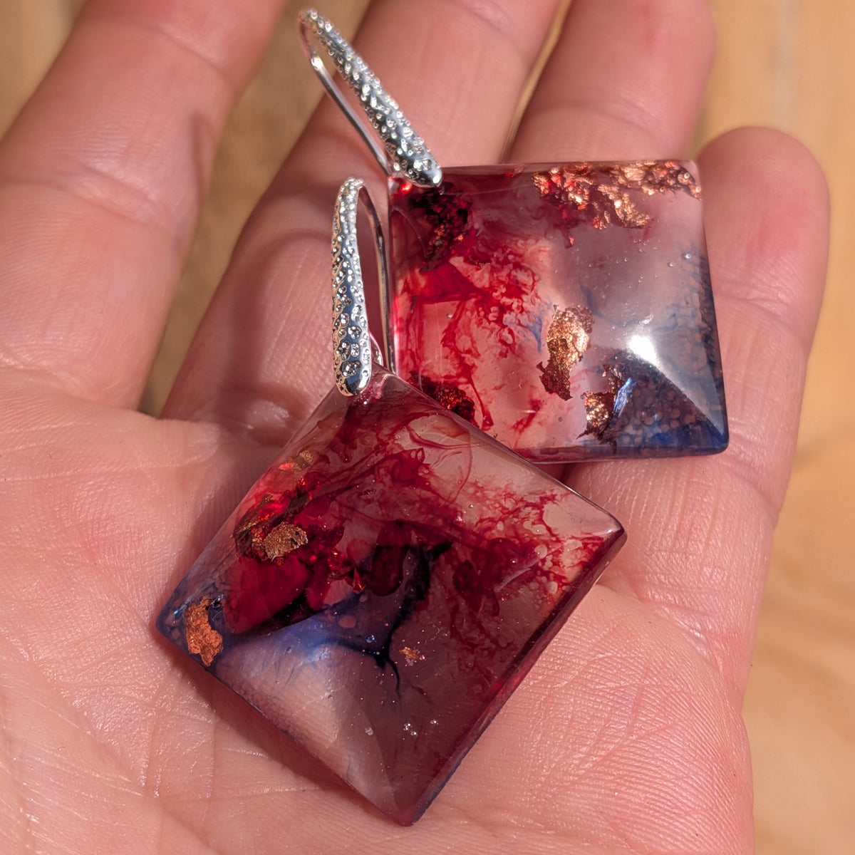 Crimson blue square earrings resting on a palm with silver hooks visible, EL-Creations