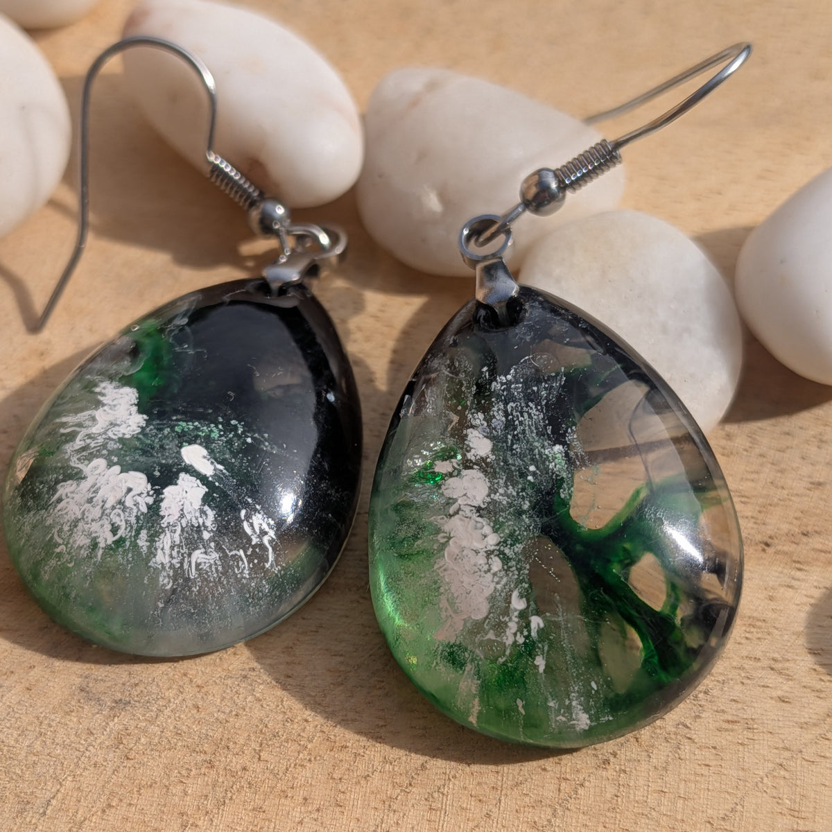 Close-up of teardrop resin earrings with stainless steel hooks beside white stones, EL-Creations
