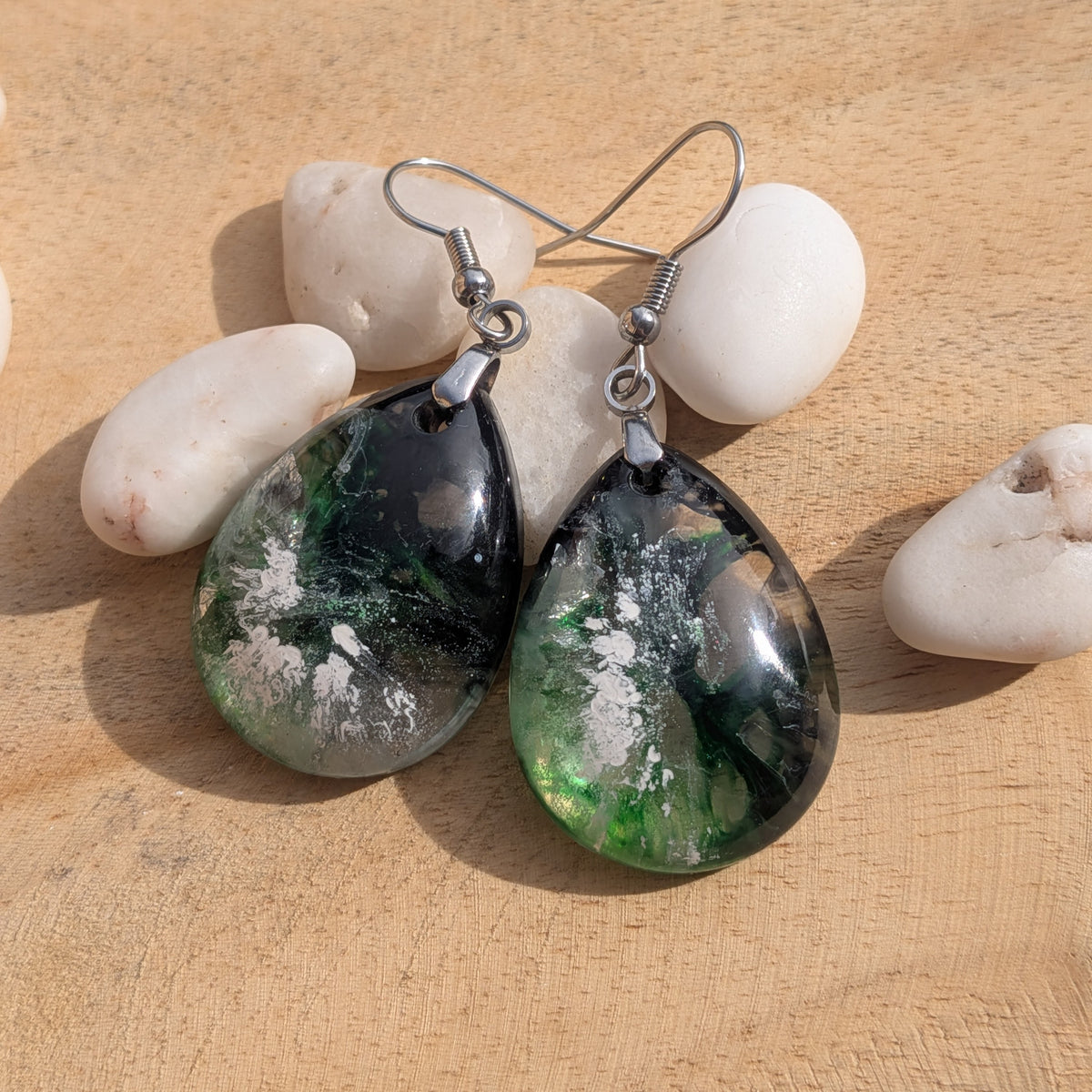 Pair of emerald green black teardrop earrings arranged on wood with white stones, EL-Creations