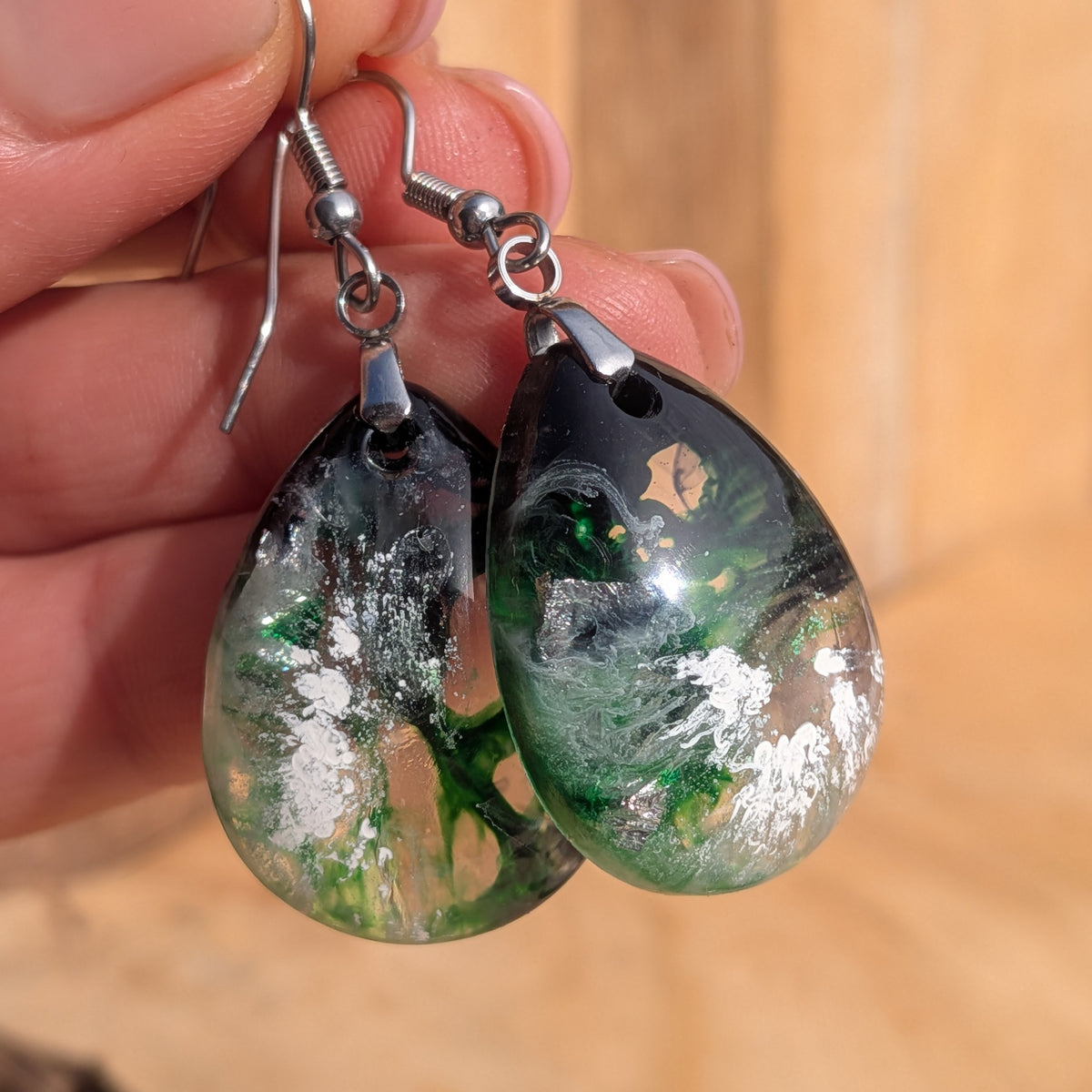 Green and black teardrop resin earrings with stainless steel hooks held in hand, EL-Creations