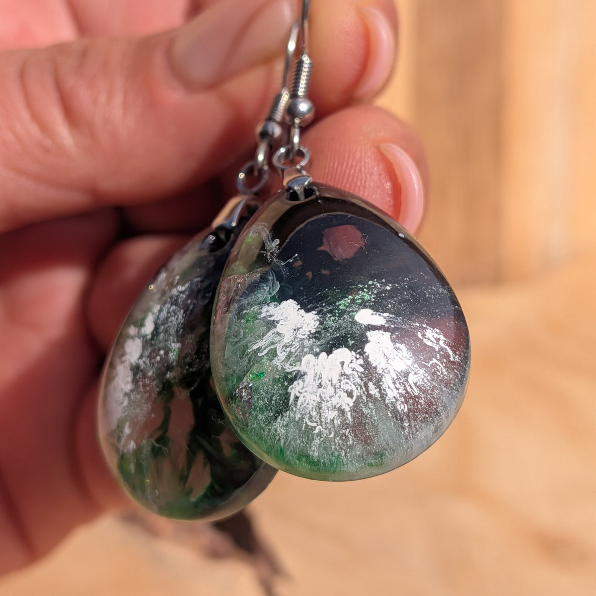 Macro view of glossy green black resin earrings with pale abstract details, EL-Creations
