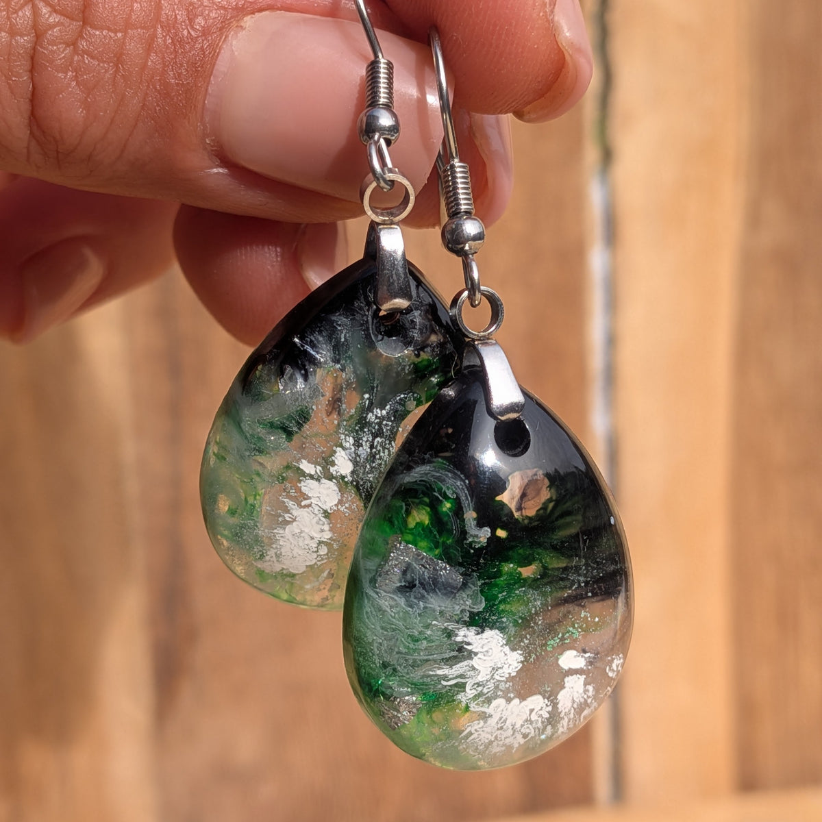 Front view of green black teardrop resin earrings against a wooden background, EL-Creations