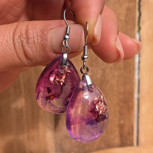 Purple pink teardrop resin earrings with stainless steel hooks held against wood, EL-Creations