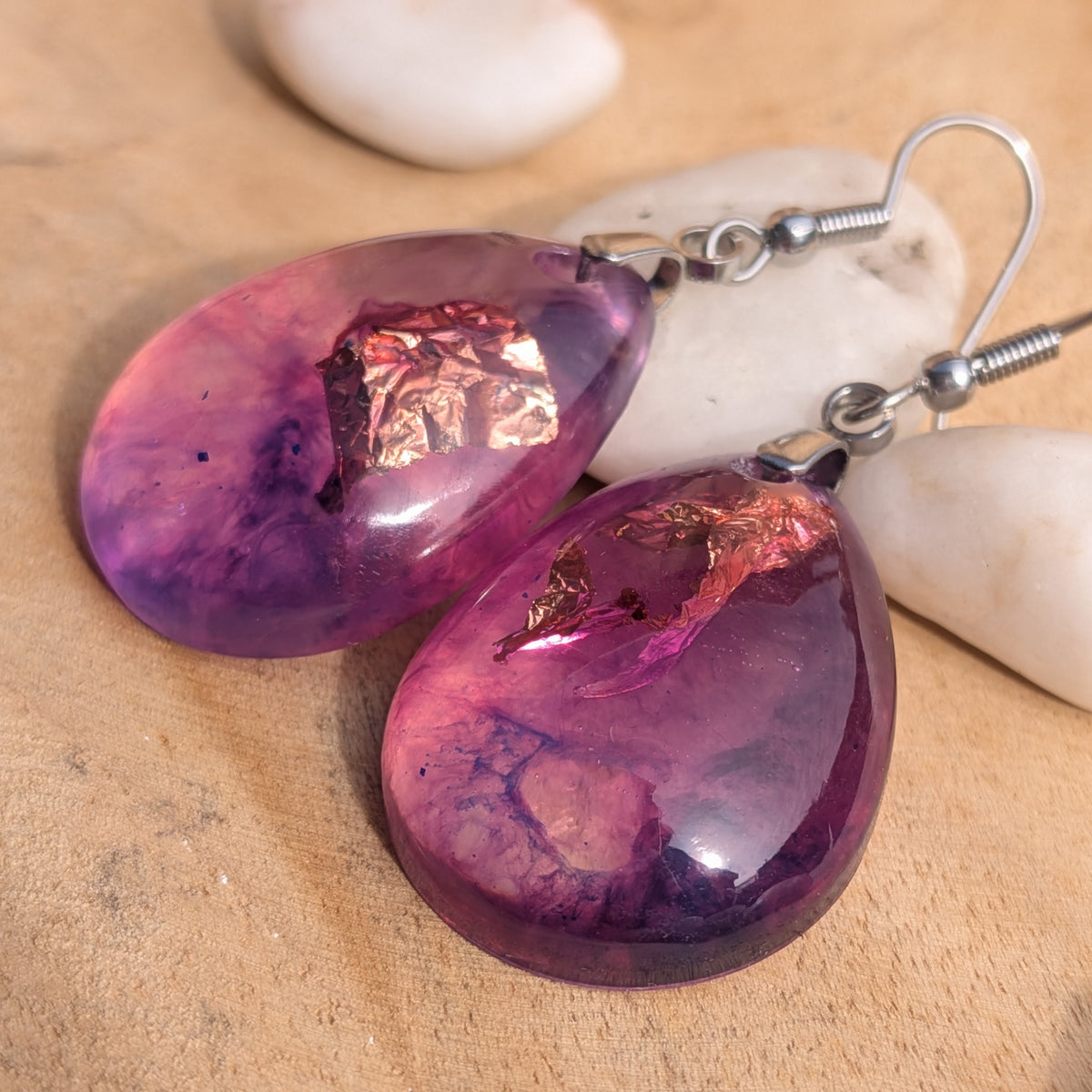 Purple pink resin earrings lying on wood beside white stones, EL-Creations