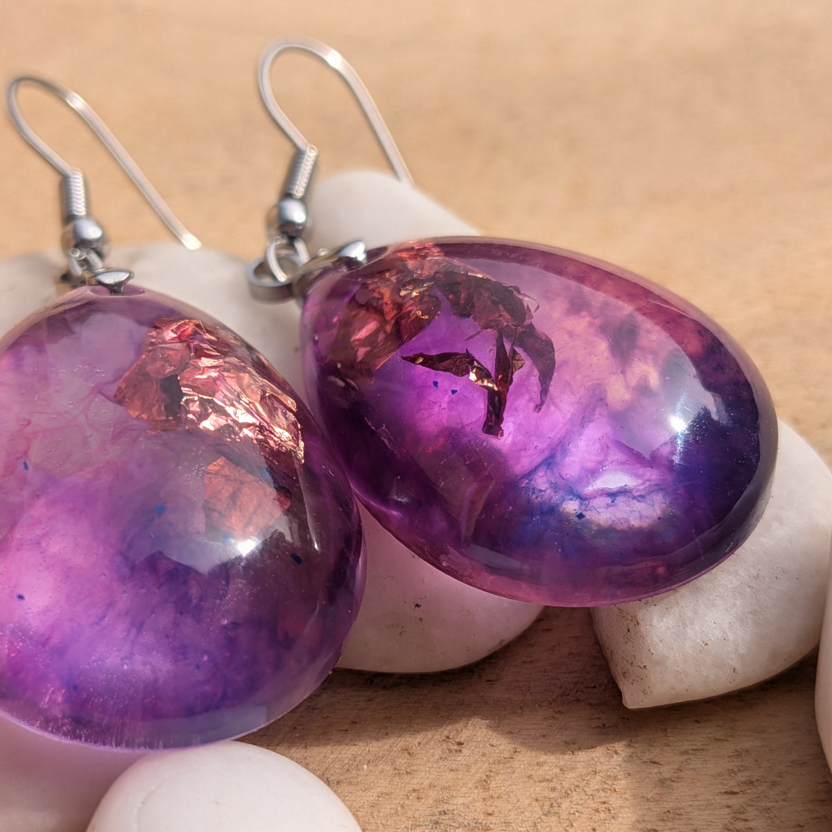Close-up of purple pink teardrop earrings showing abstract swirls and warm metallic-coloured accents, EL-Creations