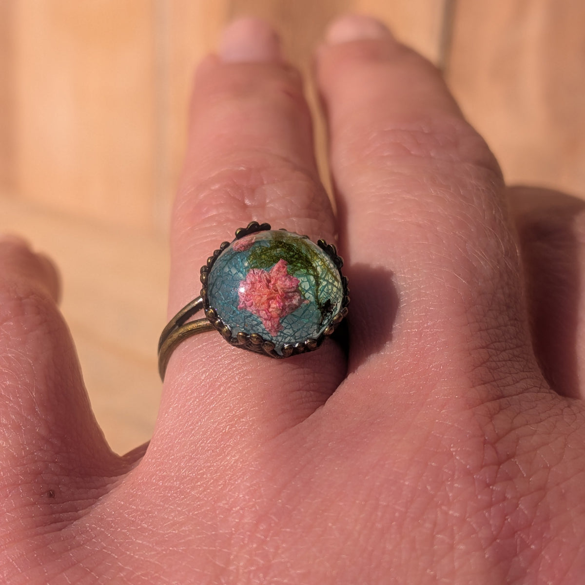 Pink baby’s breath and moss resin ring worn on a finger at an angle, with its rustic brown split band visible, EL-Creations