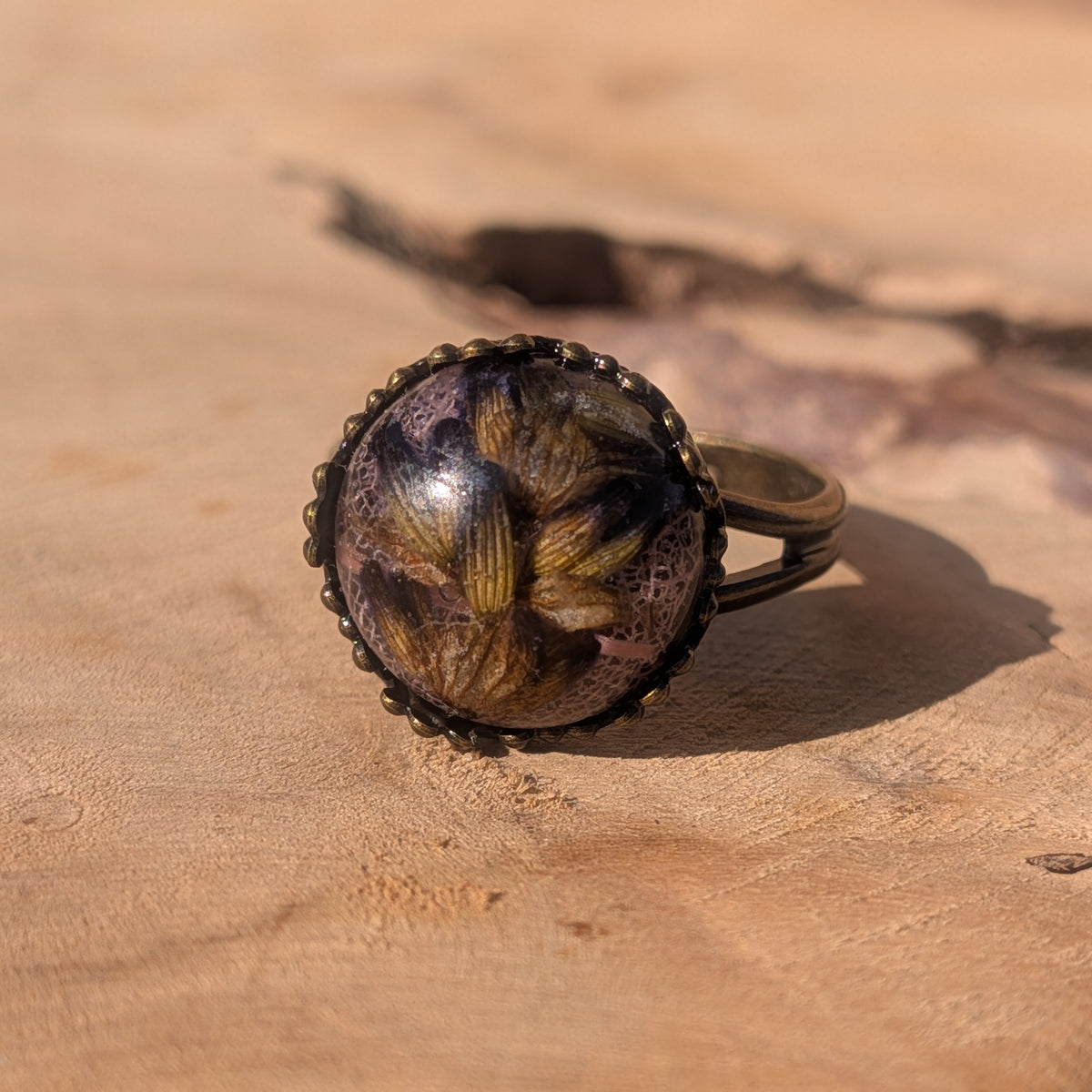 Close-up front view of lavender preserved over pink skeleton leaf inside a glossy resin ring with a rustic brown border, EL-Creations