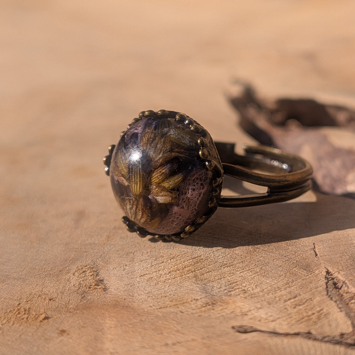 Angled view of a lavender botanical resin ring on wood, showing its open adjustable band and delicate pink leaf veins, EL-Creations