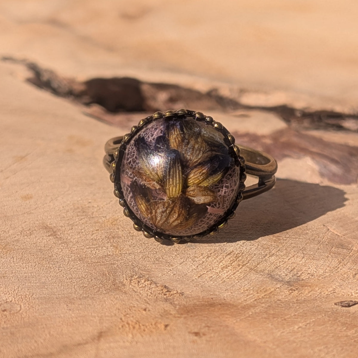 Lavender and pink skeleton leaf resin ring displayed on a wooden surface, with preserved botanical details visible beneath the glossy dome, EL-Creations