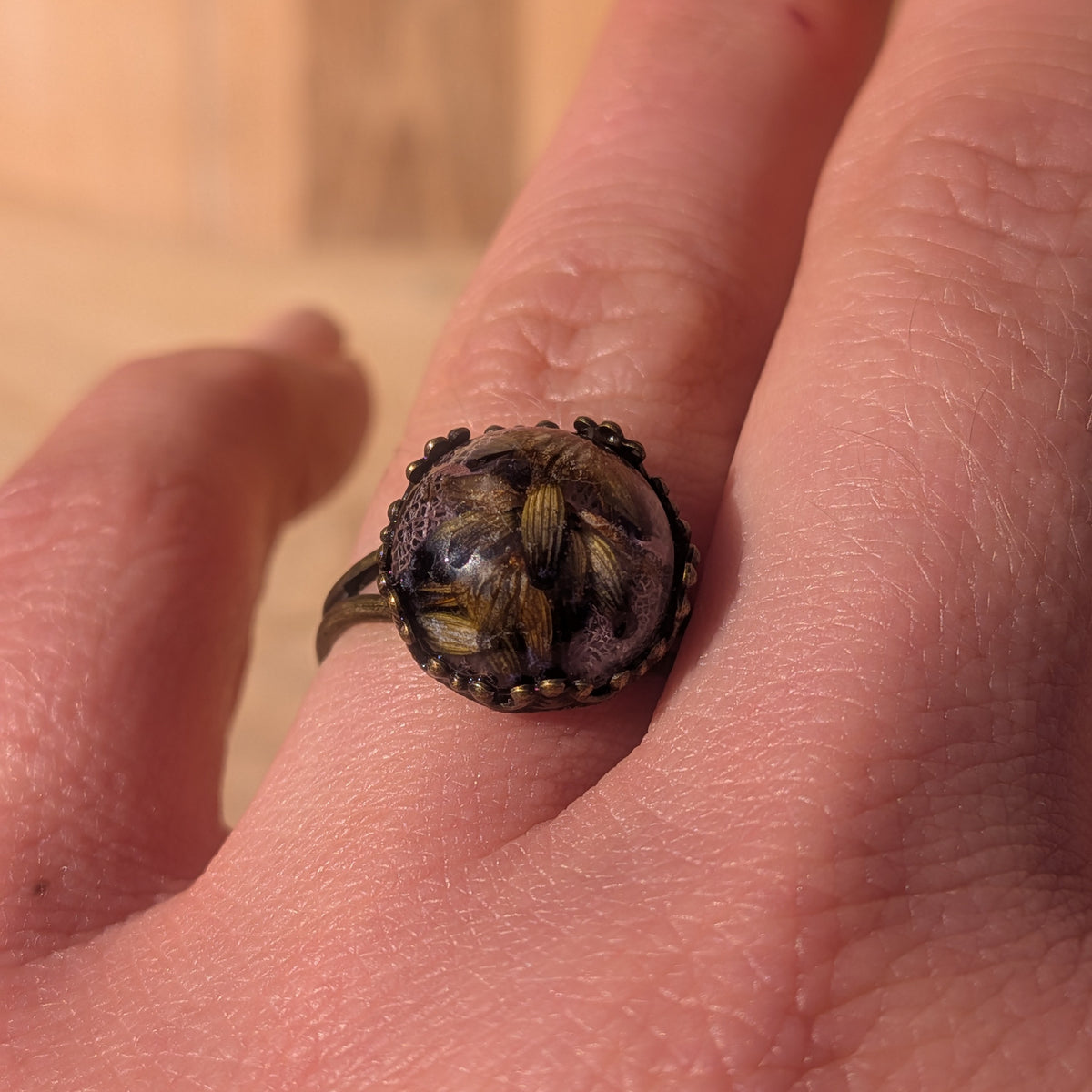 Macro view of a lavender and pink skeleton leaf resin ring worn on a finger in sunlight, EL-Creations