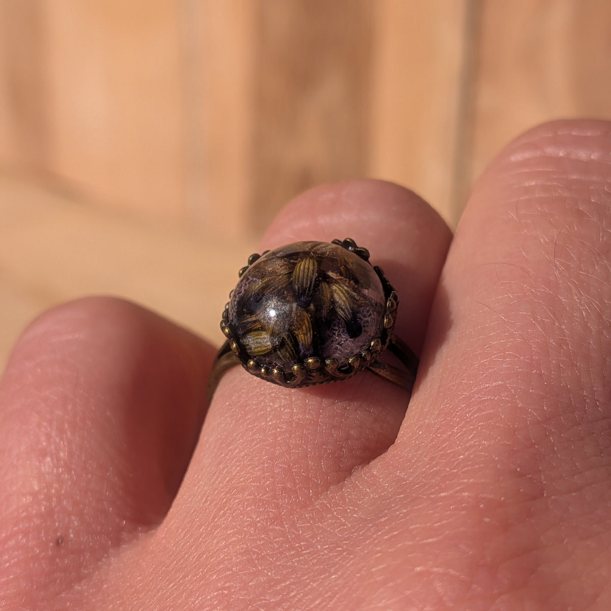 Close-up of lavender and fine pink skeleton leaf veins preserved in a domed resin ring worn on a finger, EL-Creations