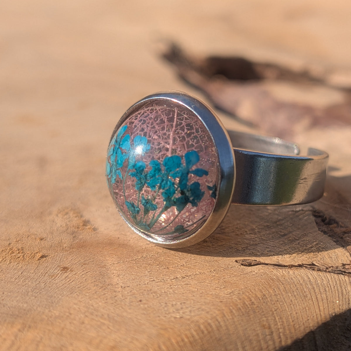 Angled view of a blue Queen Anne’s lace and pink leaf resin ring, showing its open adjustable stainless steel band, EL-Creations