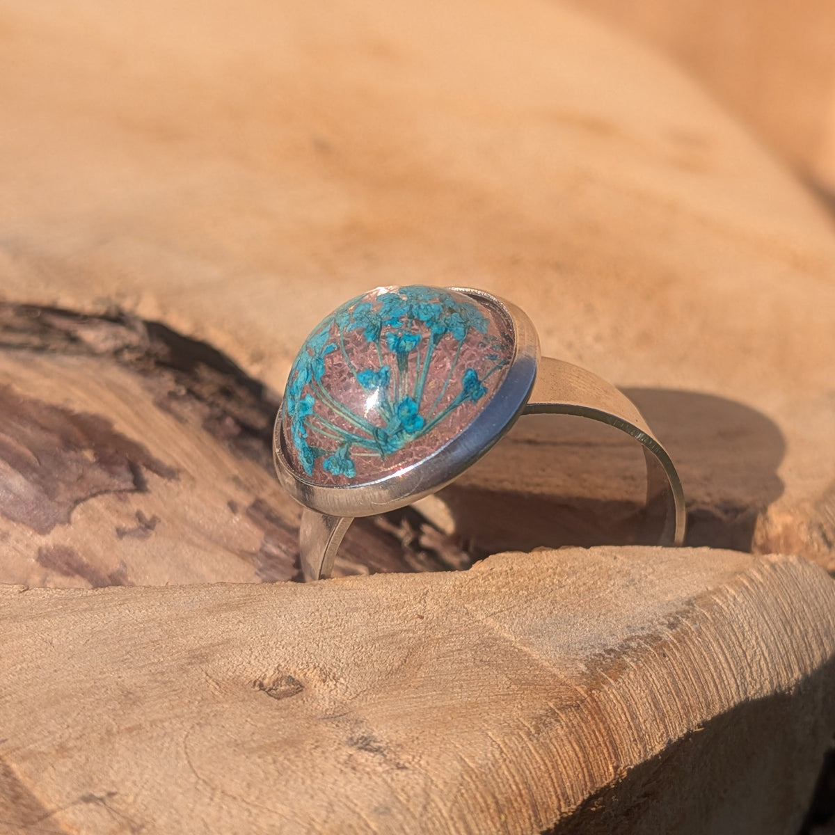 Side view of a botanical resin ring standing in a crack in wood, showing its glossy dome and stainless steel setting, EL-Creations