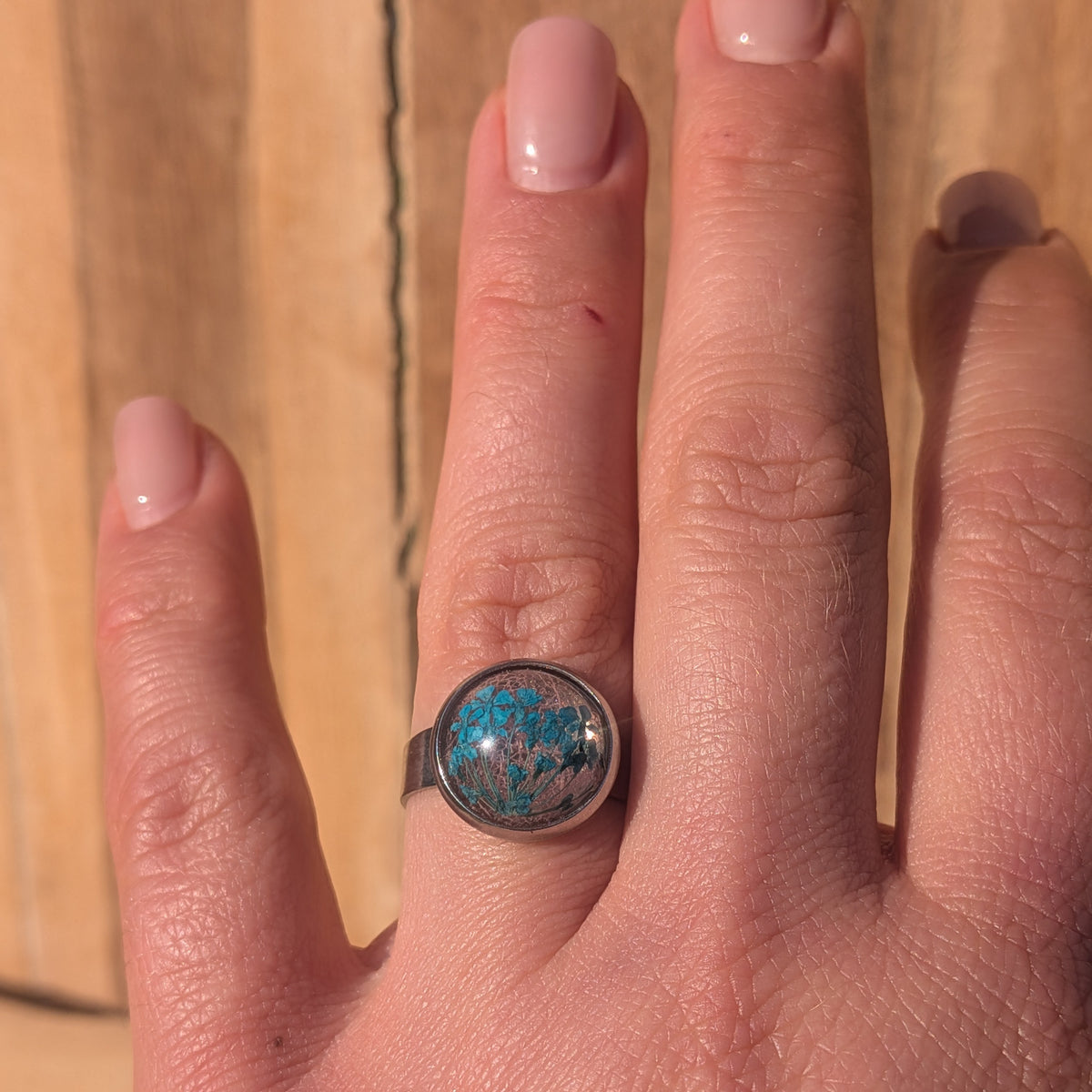 Blue Queen Anne’s lace and pink skeleton leaf resin ring worn on an outstretched hand against a wooden background, EL-Creations