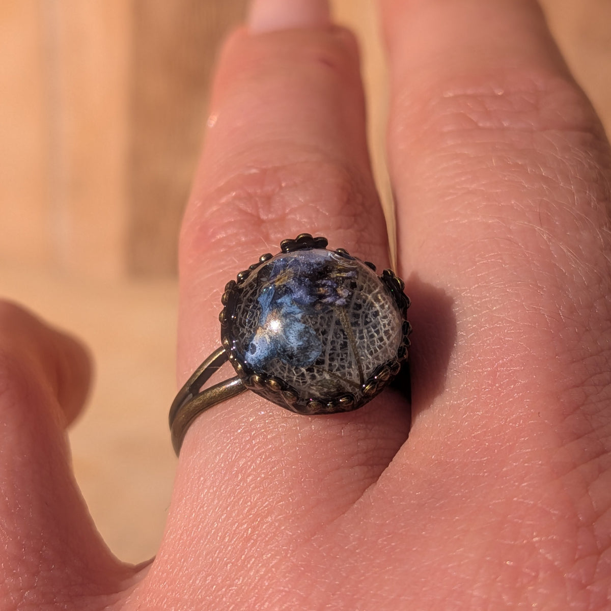 Adjustable forget-me-not and white leaf resin ring worn on a finger at an angle, with its rustic brown split band visible, EL-Creations