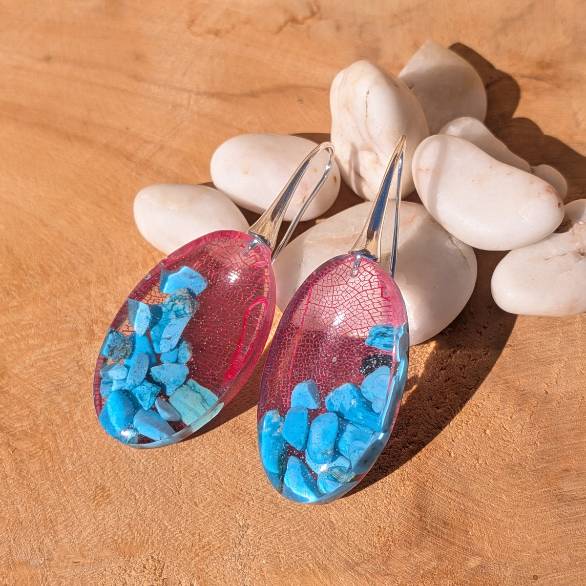 Oval red skeleton leaf and turquoise resin earrings lying flat on a wooden surface, EL-Creations