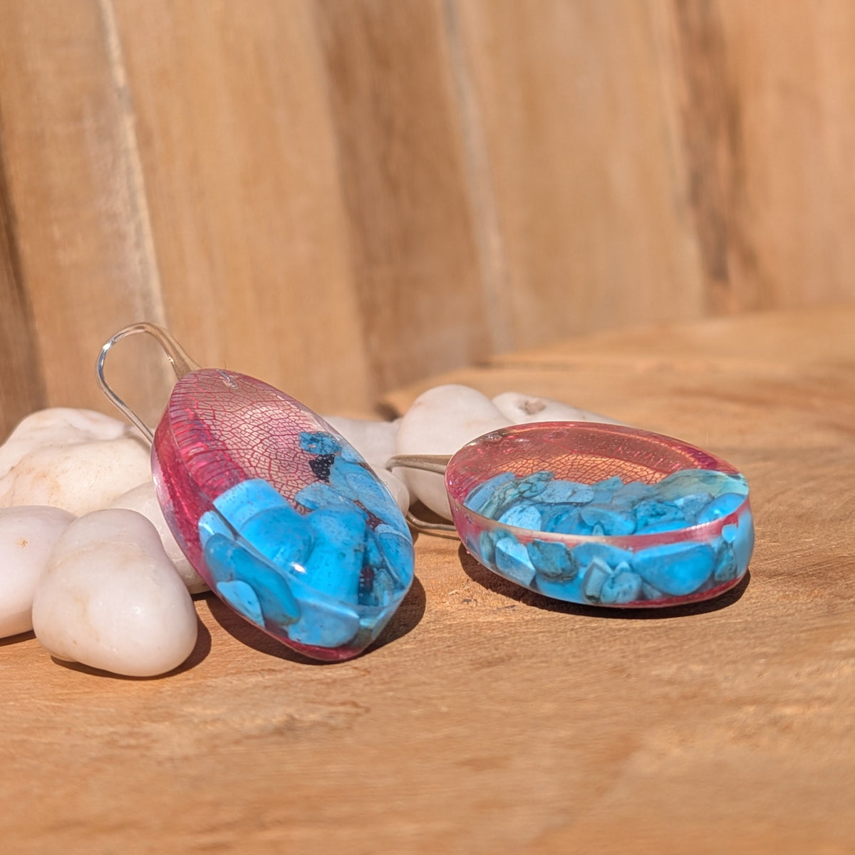 Handmade oval resin earrings with red skeleton leaves and blue turquoise chips in sunlight, EL-Creations