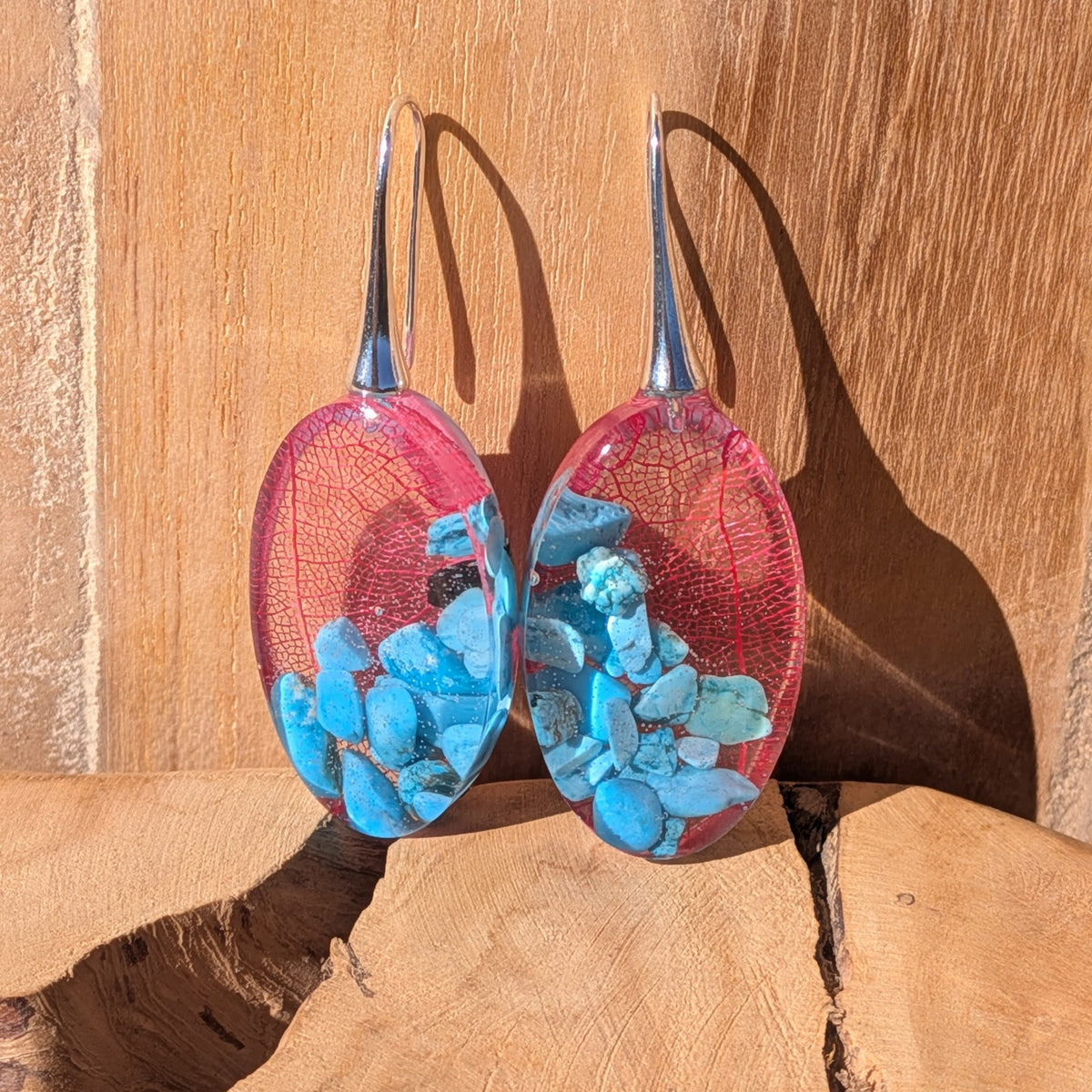 Angled view of red leaf and turquoise resin earrings with silver-tone alloy hooks beside white pebbles, EL-Creations