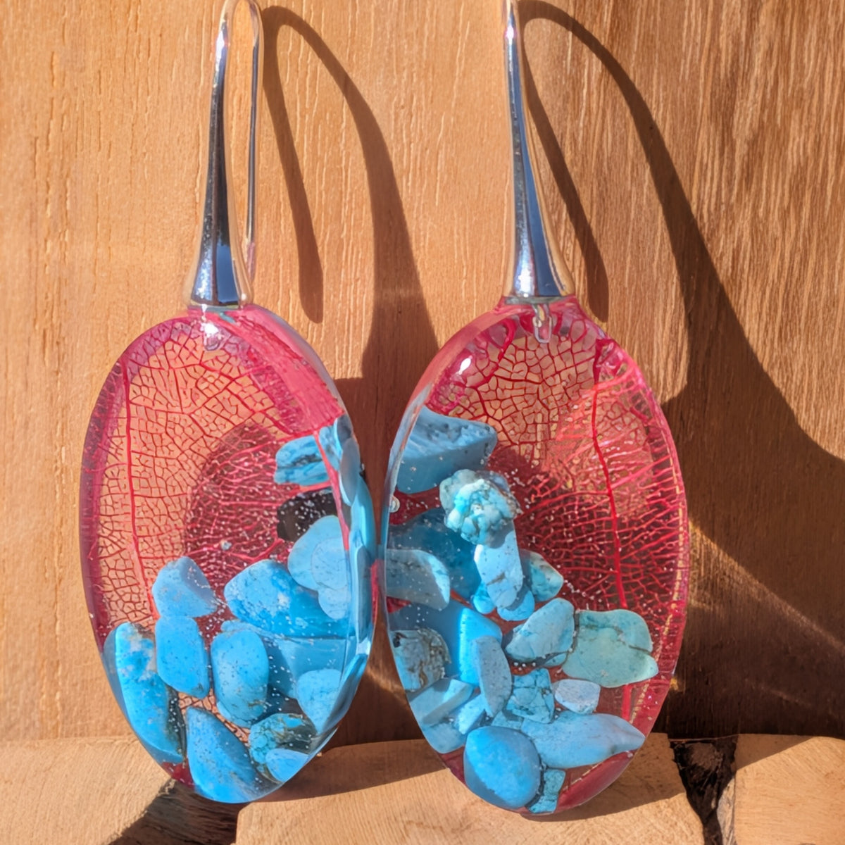 Front view of red skeleton leaf and genuine turquoise earrings against a wooden background, EL-Creations