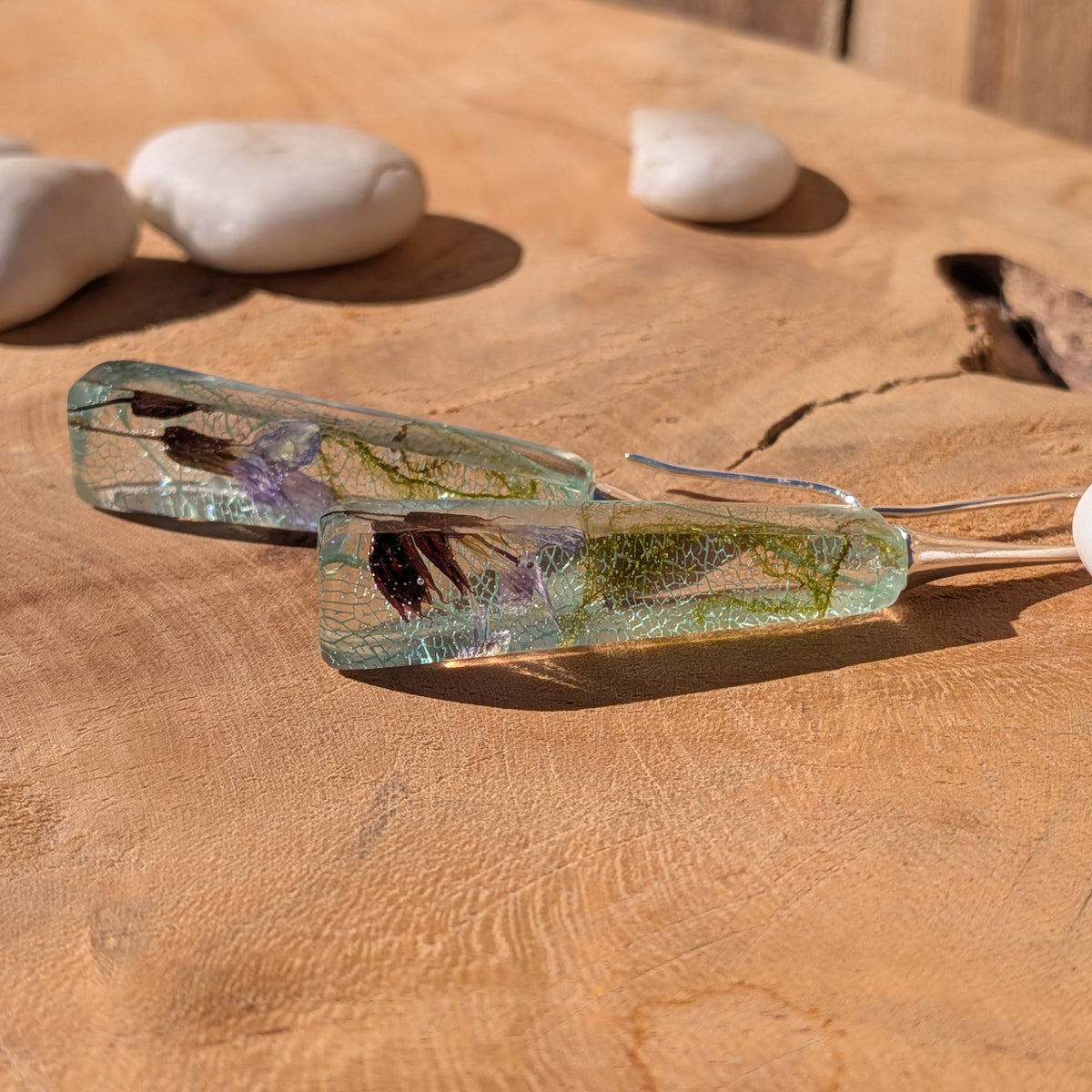 Front view of long moss and light blue skeleton leaf earrings against a wooden background, EL-Creations