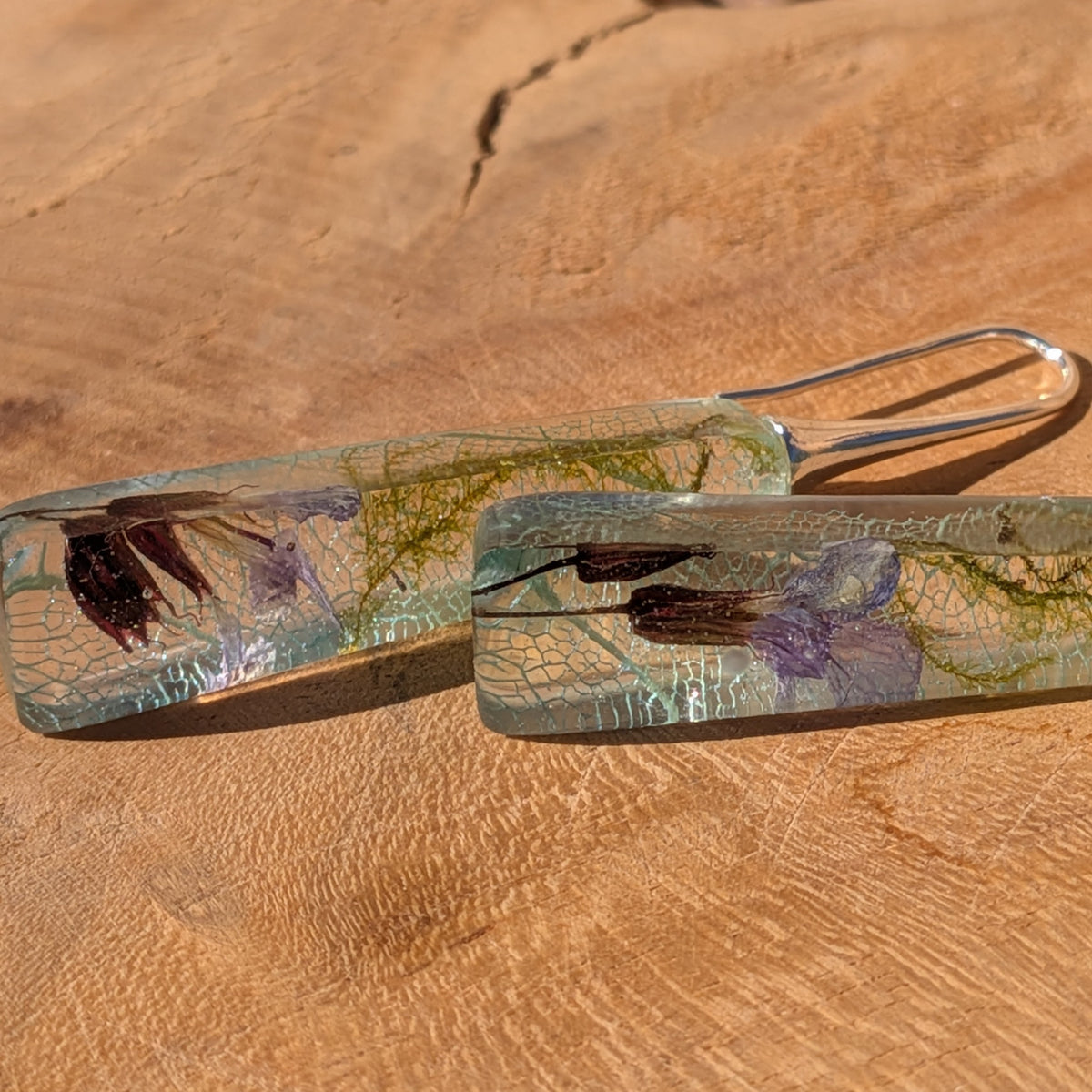 Light blue skeleton leaf and moss resin earrings resting on white stones in sunlight, EL-Creations