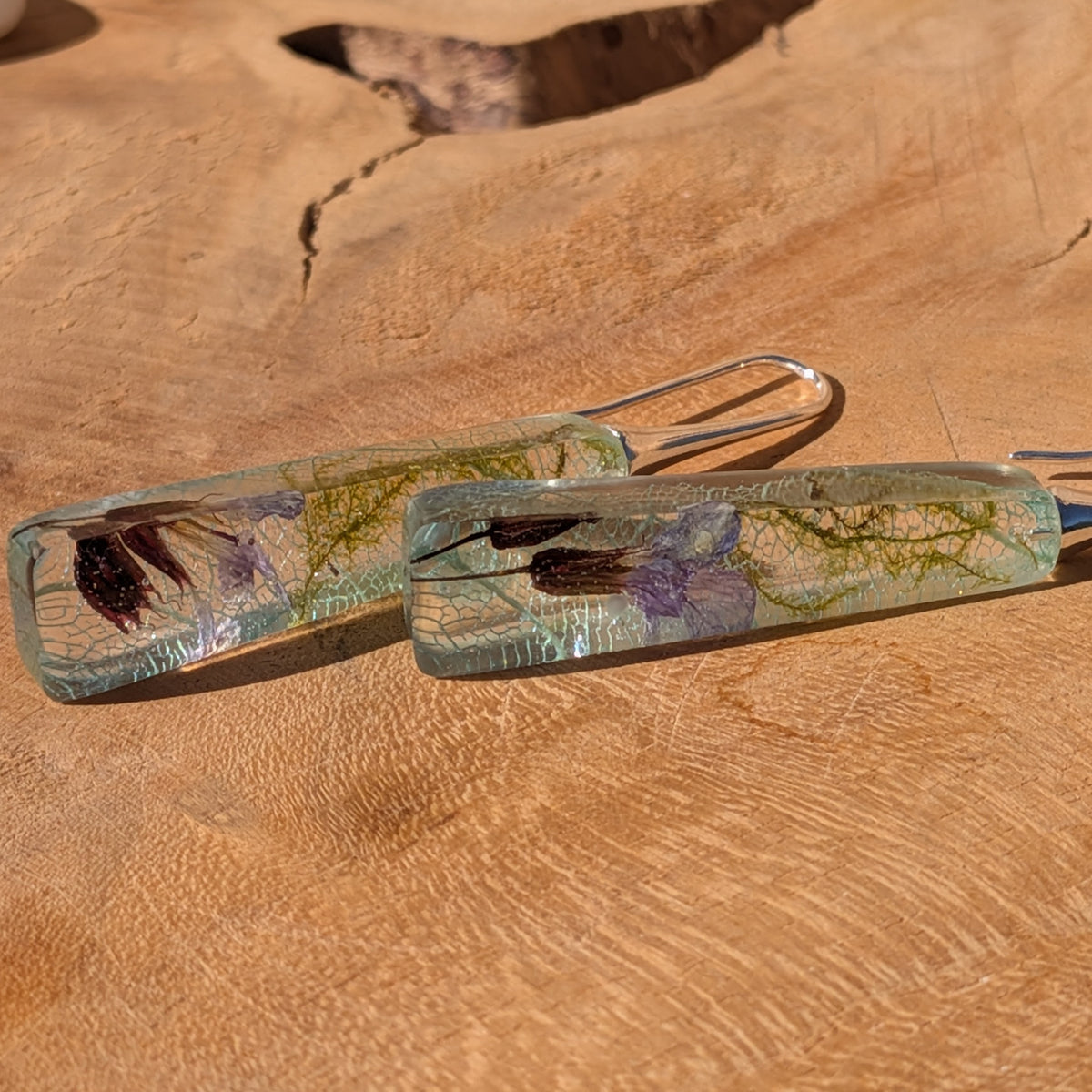 Angled view of tapered resin earrings with green moss and delicate light blue leaf patterns, EL-Creations