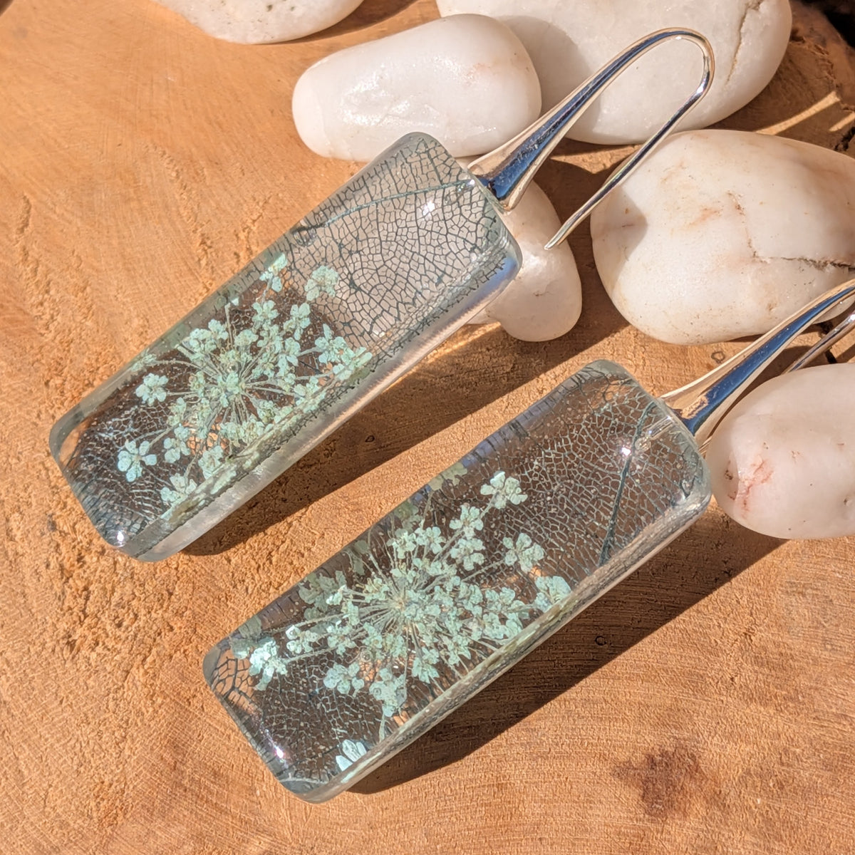 Pair of botanical resin drop earrings with lace-like flower clusters beside white pebbles, EL-Creations