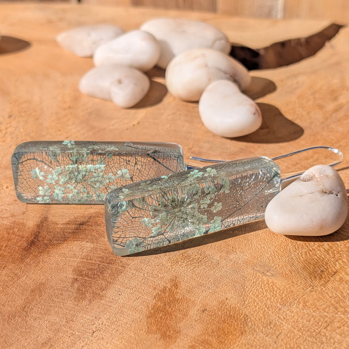 Rectangular resin earrings with Queen Anne's lace and skeleton leaf beside white stones on wood, EL-Creations