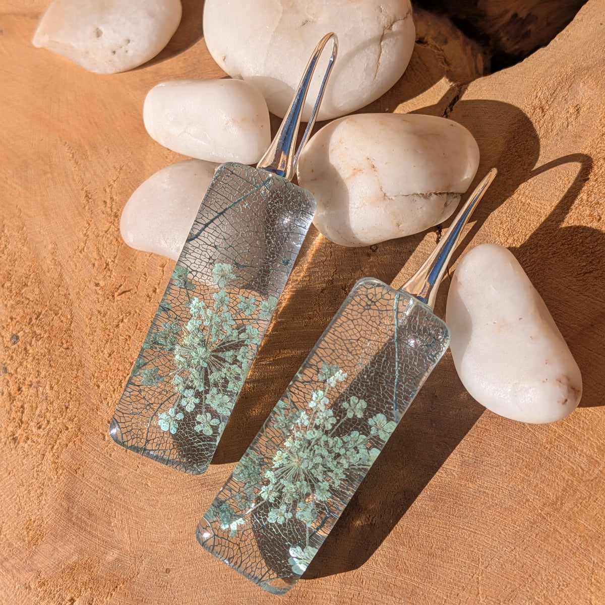 Front view of Queen Anne's lace resin earrings with intricate leaf patterns against wood, EL-Creations