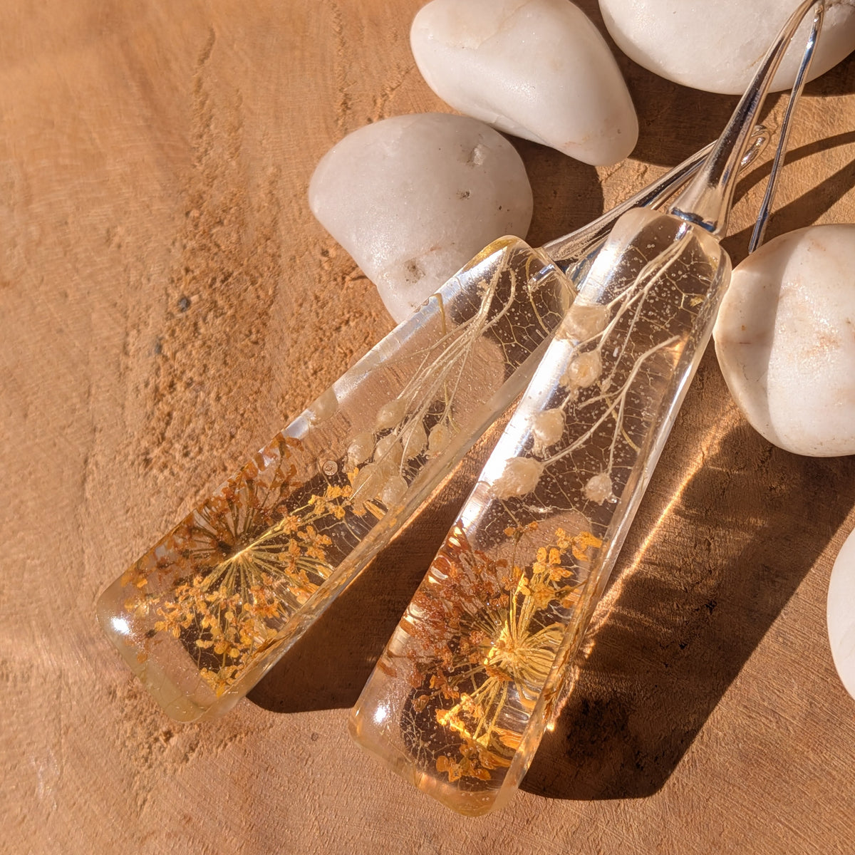 Clear resin earrings with golden Queen Anne's lace and pale wildflowers beside white stones, EL-Creations⠋