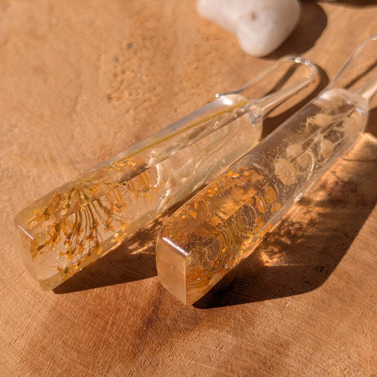 Overhead view of autumn resin drop earrings with golden flowers and pale wildflower stems, EL-Creations