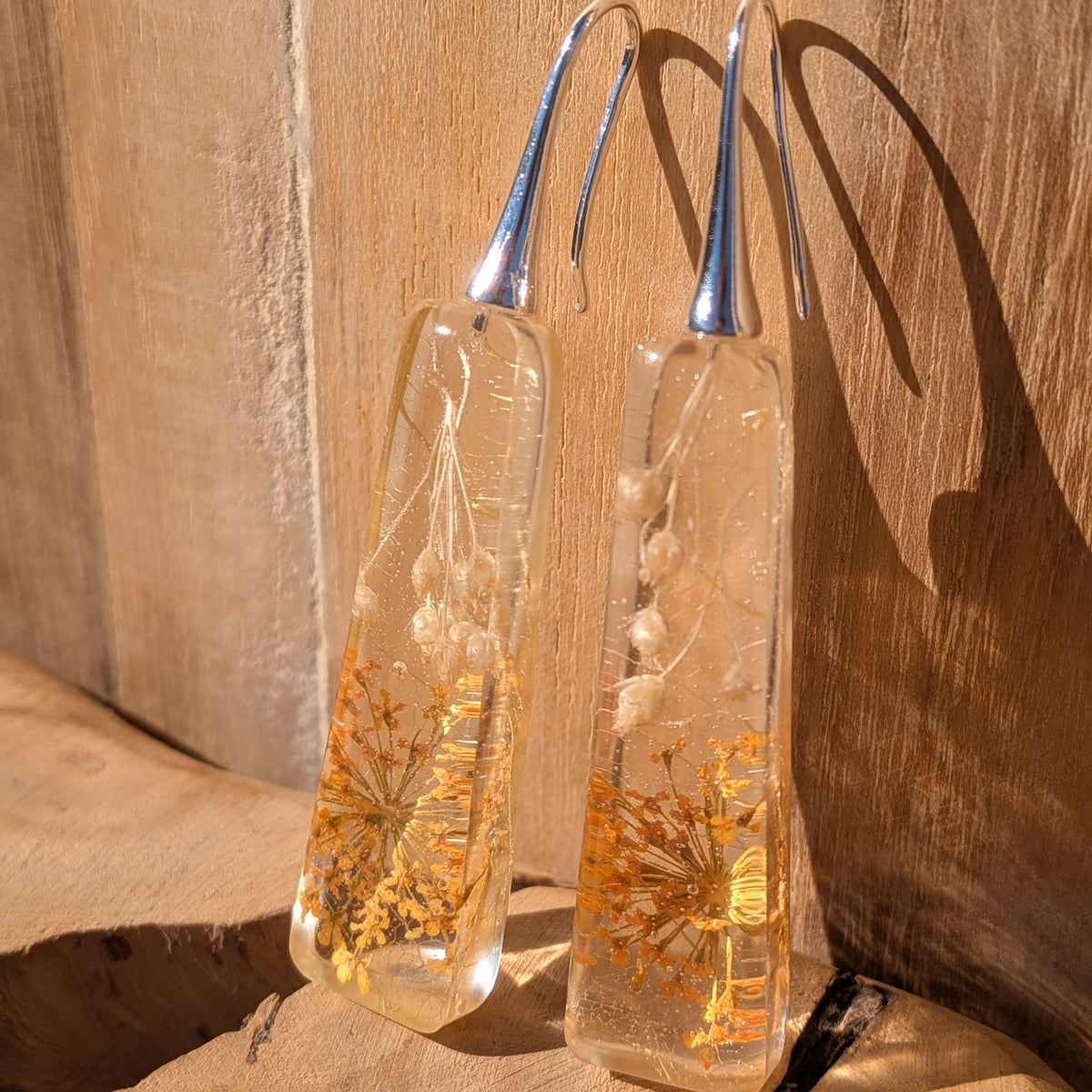 Front view of long Queen Anne's lace and wildflower resin earrings against wood, EL-Creations