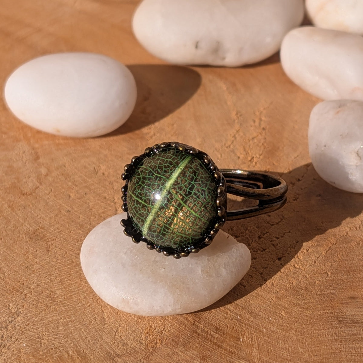 Angled view of a green leaf resin ring balanced on a white stone, with white pebbles in the background, EL-Creations