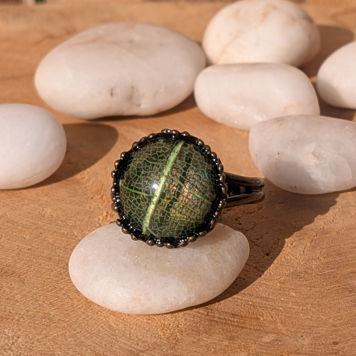 Front view of a Forest Lace resin ring on a white pebble, showing the central green leaf vein beneath its glossy dome, EL-Creations