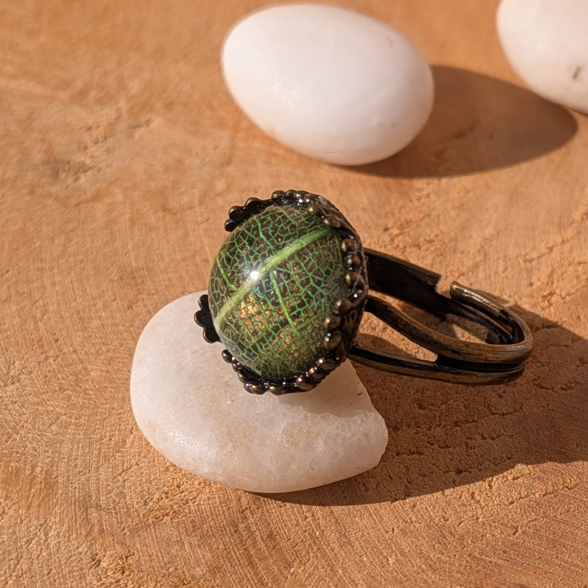 Side view of an adjustable green botanical resin ring on a white stone, showing its open brown alloy band and raised cabochon, EL-Creations