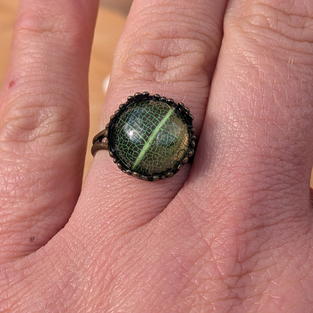 Front close-up of a green botanical resin ring worn on a finger, showing fine branching leaf veins beneath the glossy surface, EL-Creations