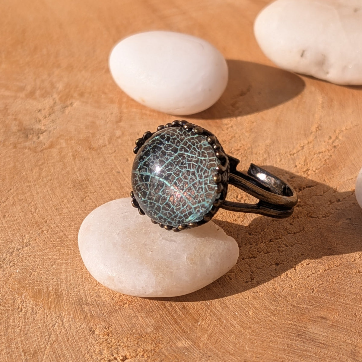 Angled view of a pale turquoise-green botanical resin ring on a white stone, showing its open adjustable brown alloy band, EL-Creations