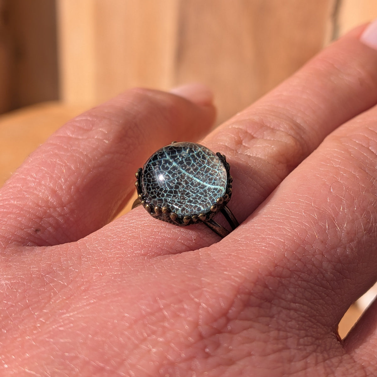 Angled close-up of a pale turquoise-green leaf vein resin ring worn on a finger in sunlight, EL-Creations