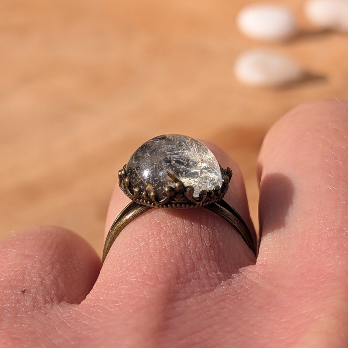 Low side view of a dandelion resin ring worn on a finger, showing its domed centre and decorative brown border, EL-Creations