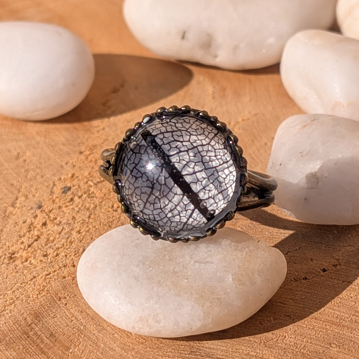Midnight Lace resin ring with intricate black skeleton leaf veins and a rustic brown setting, shown close up on a white pebble, EL-Creations